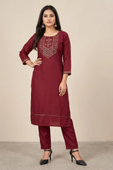 Woman wearing a maroon embroidered kurta with pants on a beige background
