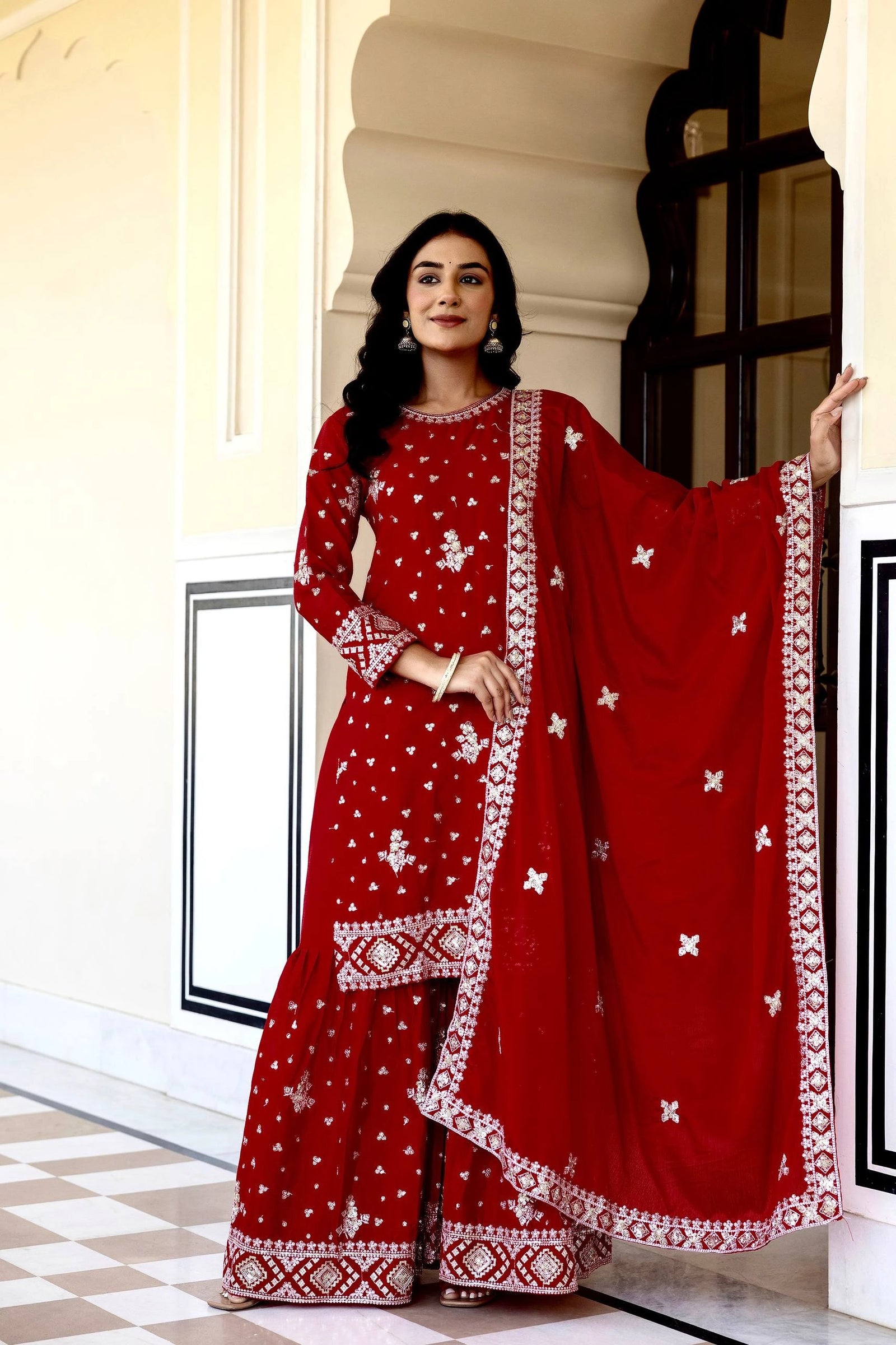 Woman in a red traditional outfit with white patterns standing in a doorway.