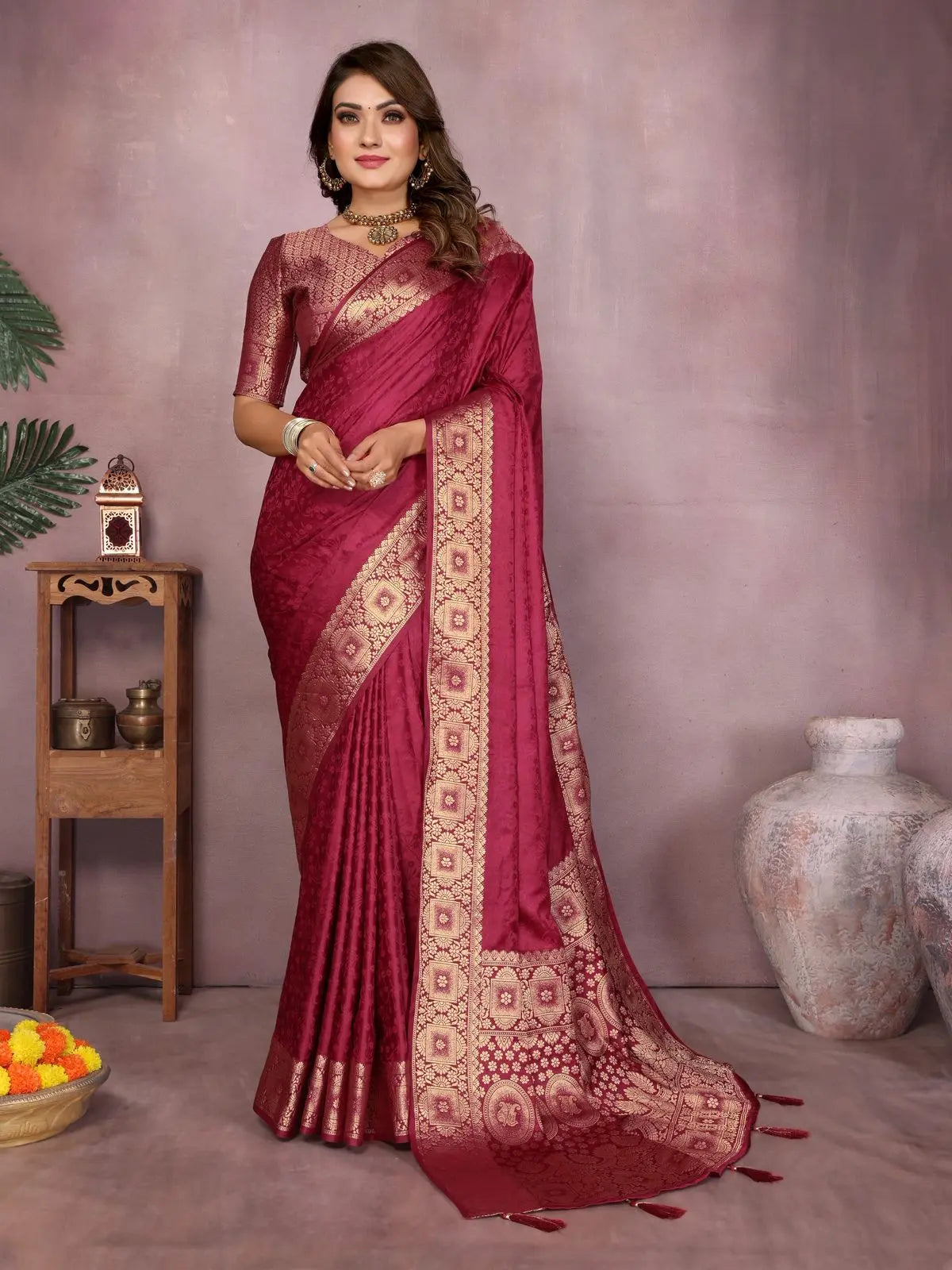Woman wearing a maroon saree with gold patterns against a neutral background