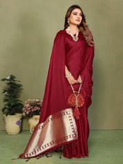 Woman in a red saree with gold border holding a matching handbag against a green background