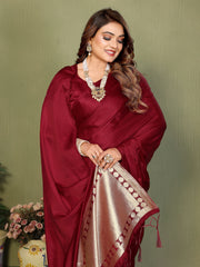 Woman wearing a maroon saree with a gold border against a green background