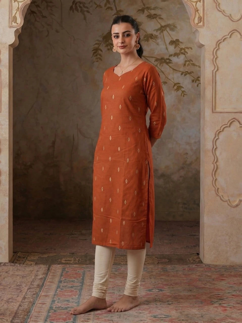 Woman wearing an orange kurta with white patterns in a decorative room.