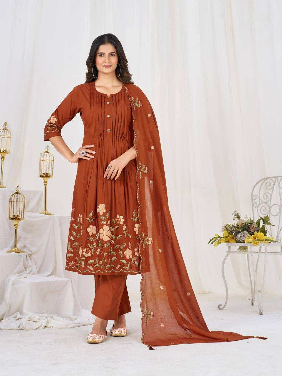 Woman wearing a brown traditional outfit with floral patterns in a decorated room.