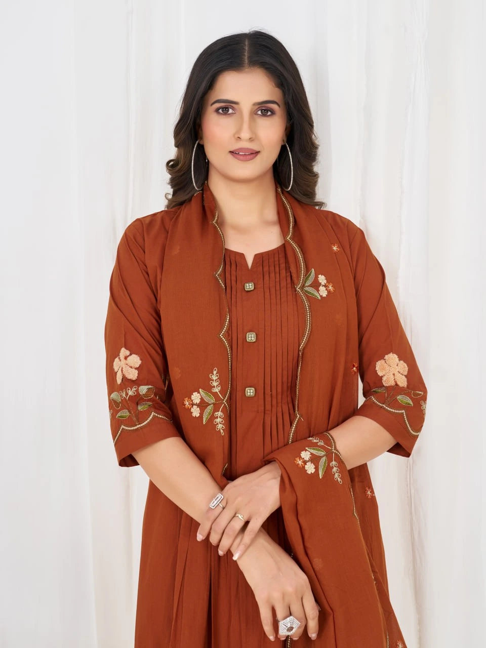 Woman wearing a rust-colored embroidered outfit against a white background