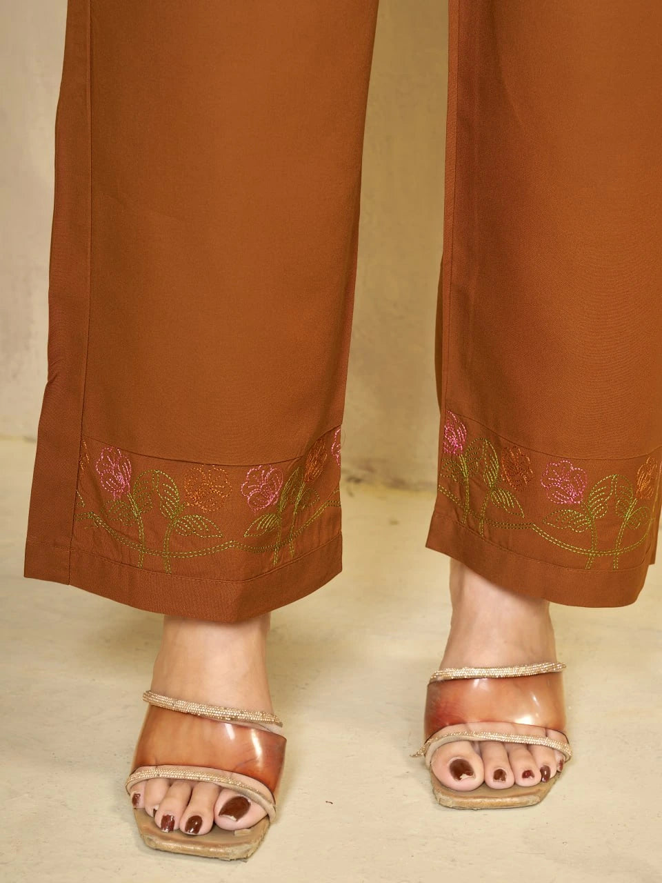 Brown pants with floral embroidery and sandals on a beige background