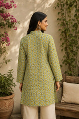 Woman wearing a green patterned kurta standing outdoors with plants and a wall in the background