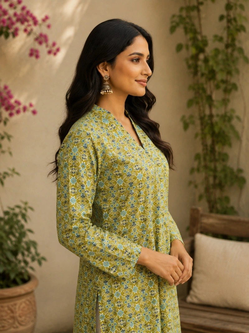 Woman wearing a green floral dress standing in a home setting with plants.