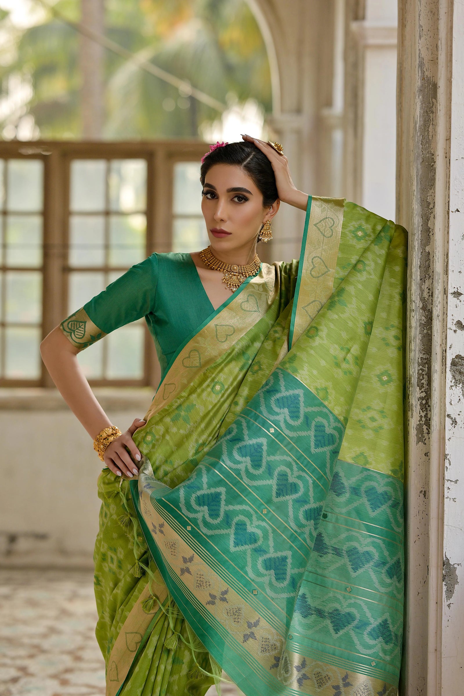 Woman wearing a green saree with a heart pattern, standing indoors.