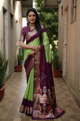 Woman wearing a green and purple saree with a patterned border in an outdoor setting.