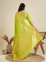 Woman wearing a bright green saree with a subtle pattern, sitting on a wooden chair against a beige background.