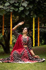 Woman in traditional red and black saree sitting on grass with yellow decorations in the background