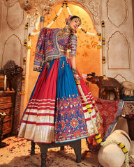 Woman in traditional Indian attire with a colorful blouse and red and blue lehenga, standing in an ornate decorated room.