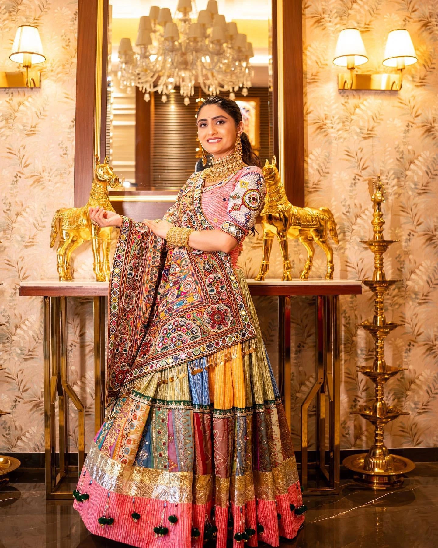 Woman in a colorful traditional outfit standing in an ornate room with gold decor.