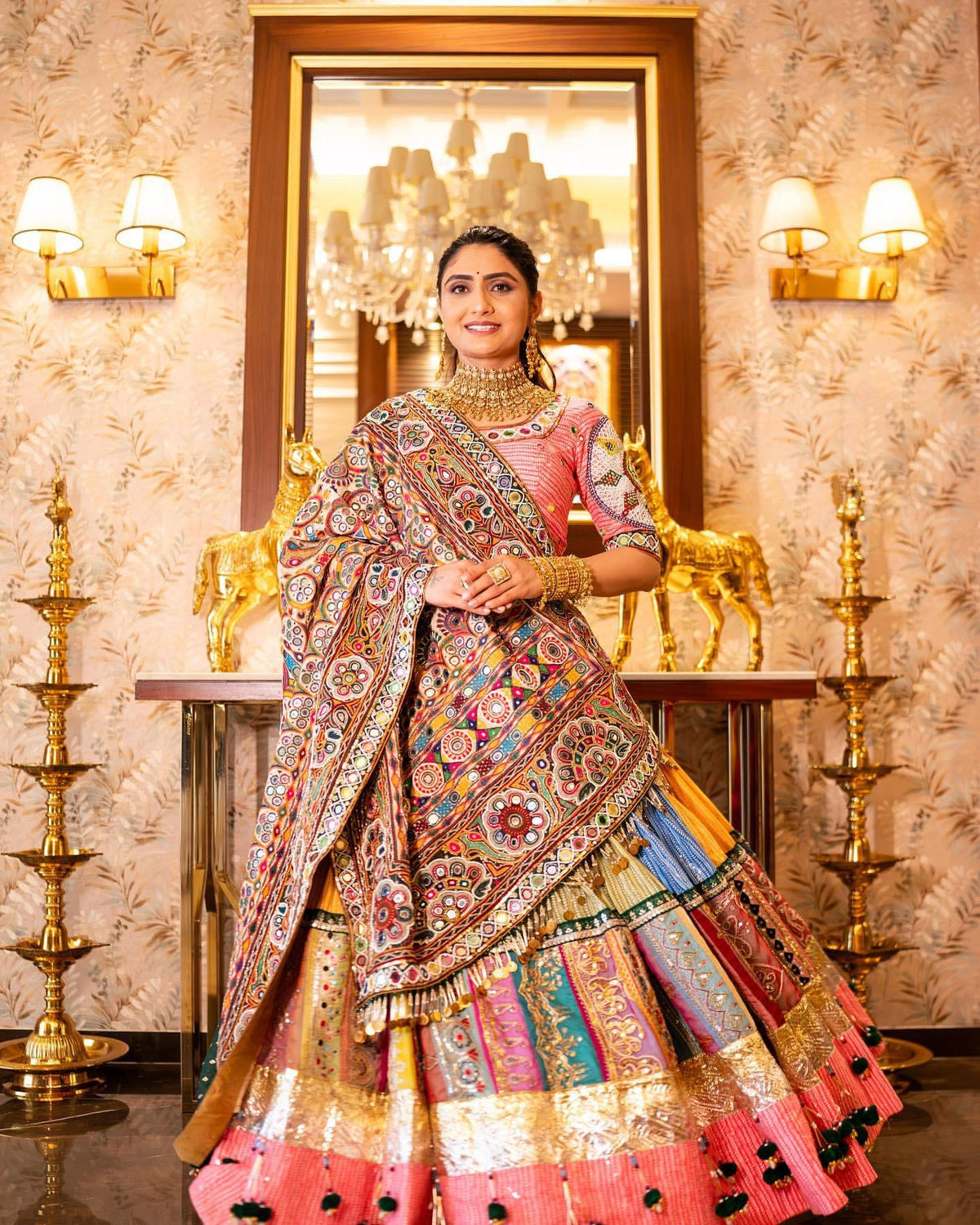 Woman in a colorful traditional outfit standing in a decorated room with mirrors and lights.