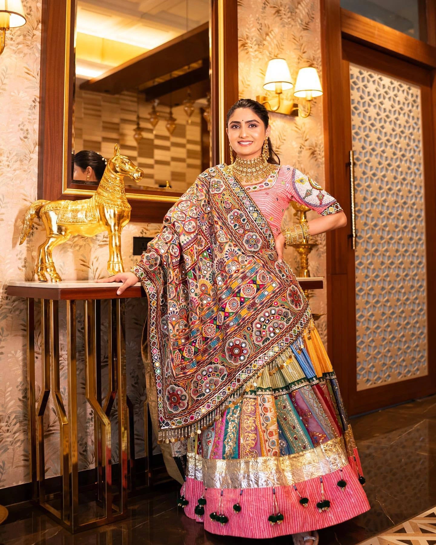 Woman in traditional multicolored outfit standing in a decorated room with decorative elements.
