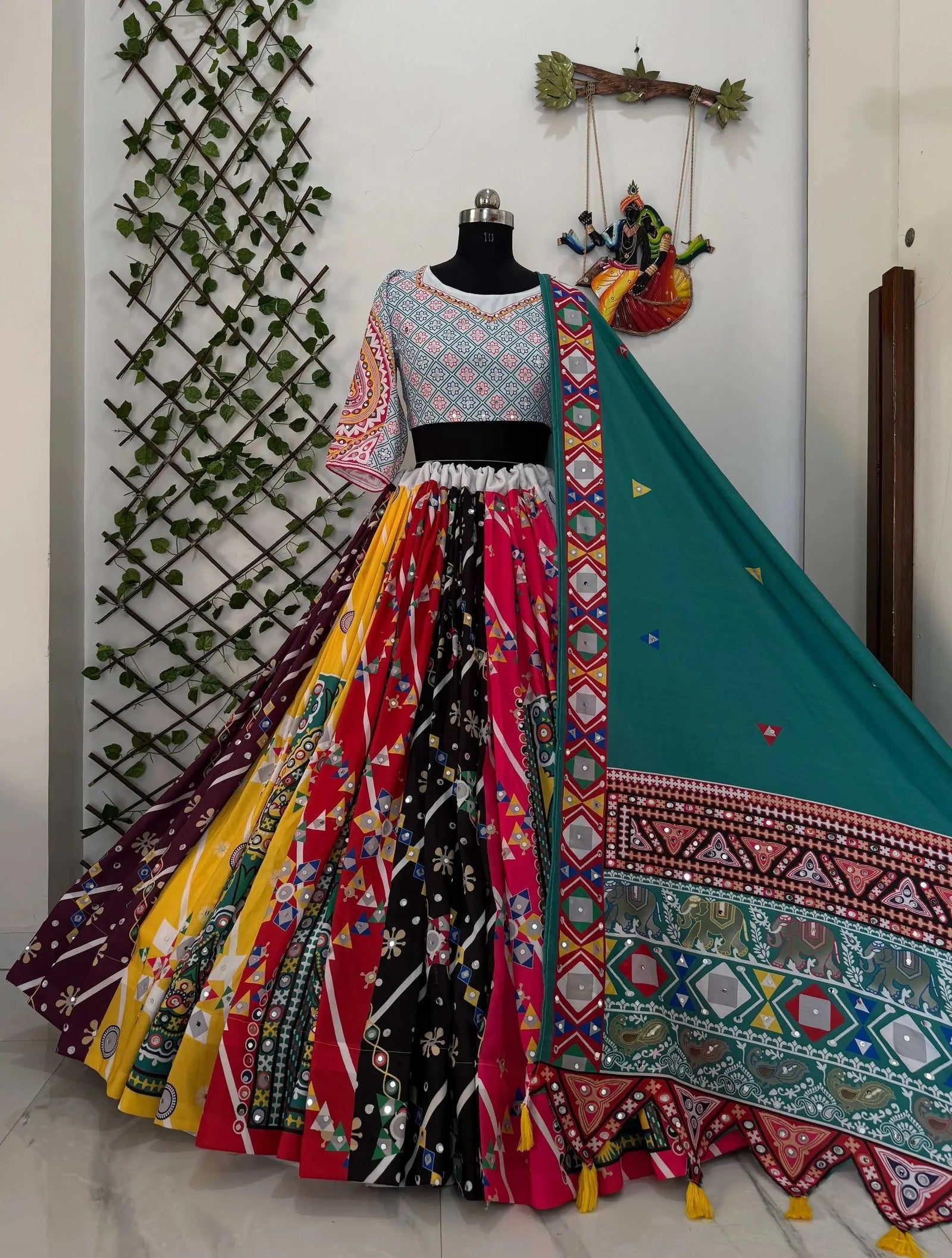 Colorful traditional outfit with a patterned dupatta on a mannequin against a decorative wall.
