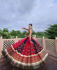 Woman in a colorful traditional outfit with a patterned skirt, standing outdoors with trees in the background.