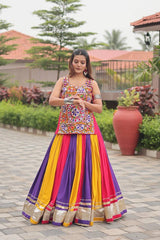 Woman in a colorful traditional outfit standing outdoors with greenery and a building in the background