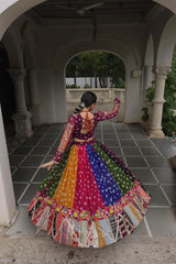 Person wearing a colorful traditional outfit in an outdoor setting with arches and greenery.