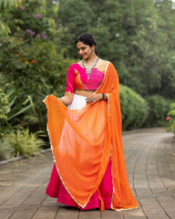 Woman in a pink and orange saree standing outdoors with greenery in the background
