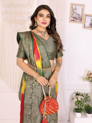 Woman in a green saree with red and yellow accents, holding a matching potli bag indoors.