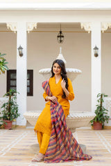 Woman in a yellow outfit holding a colorful scarf on a patio with plants and a white archway.