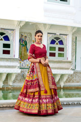 Woman in a traditional outfit with a colorful skirt and red blouse standing in front of a decorative wall.