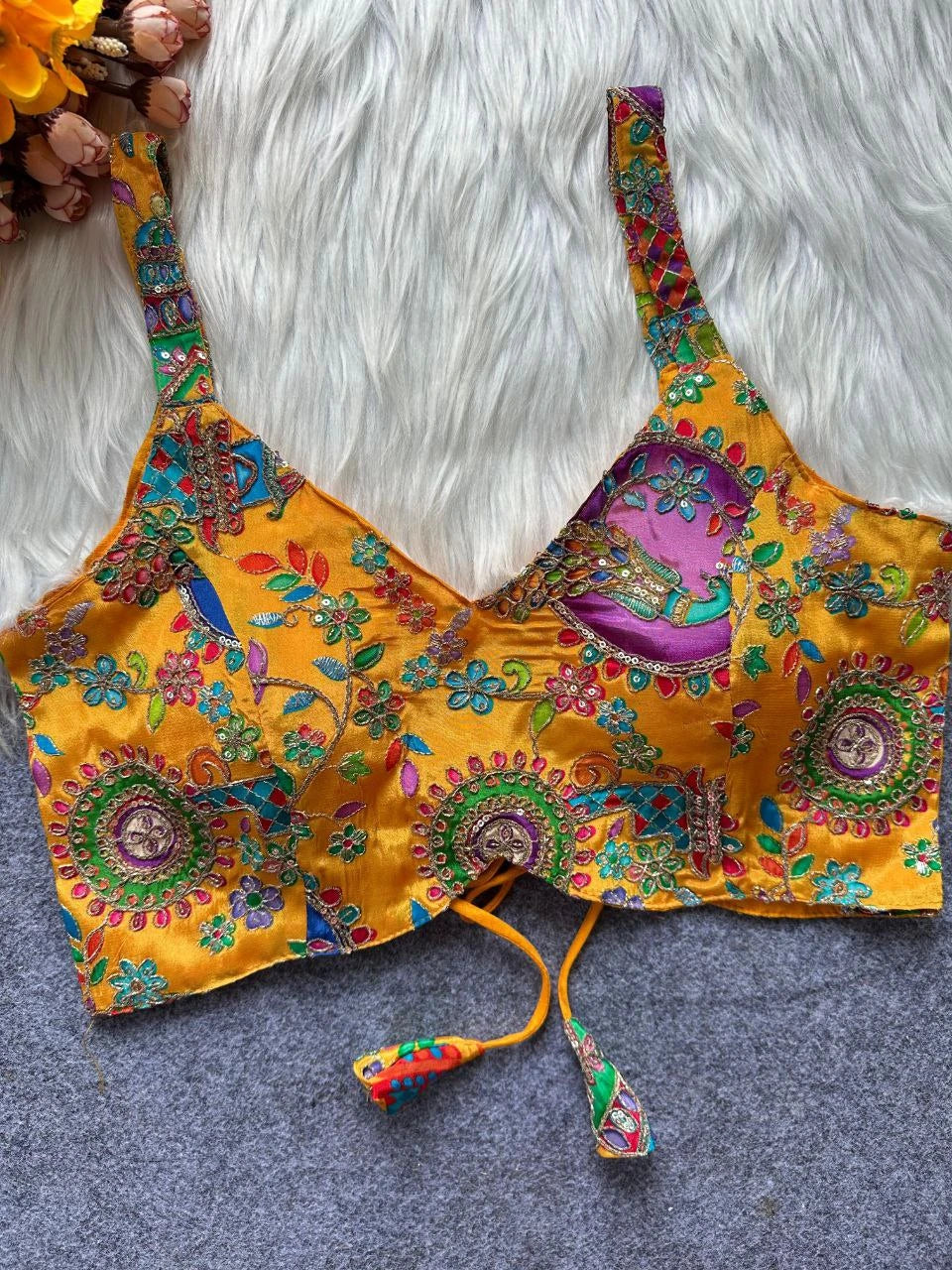 Colorful embroidered bralette on a textured surface with flowers in the background