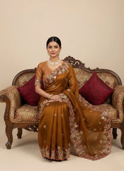 Woman in a brown saree sitting on an ornate couch with red cushions.