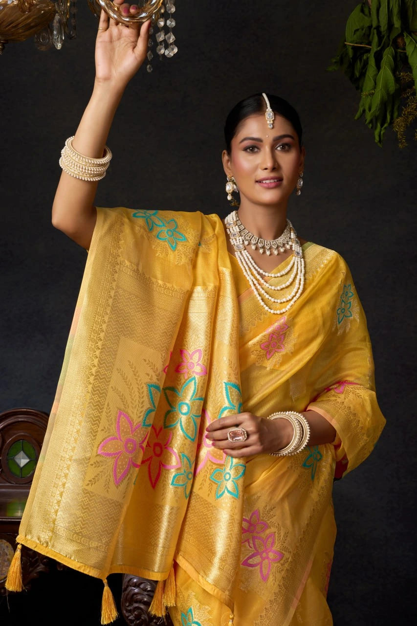 Woman wearing a yellow saree with floral patterns against a dark background
