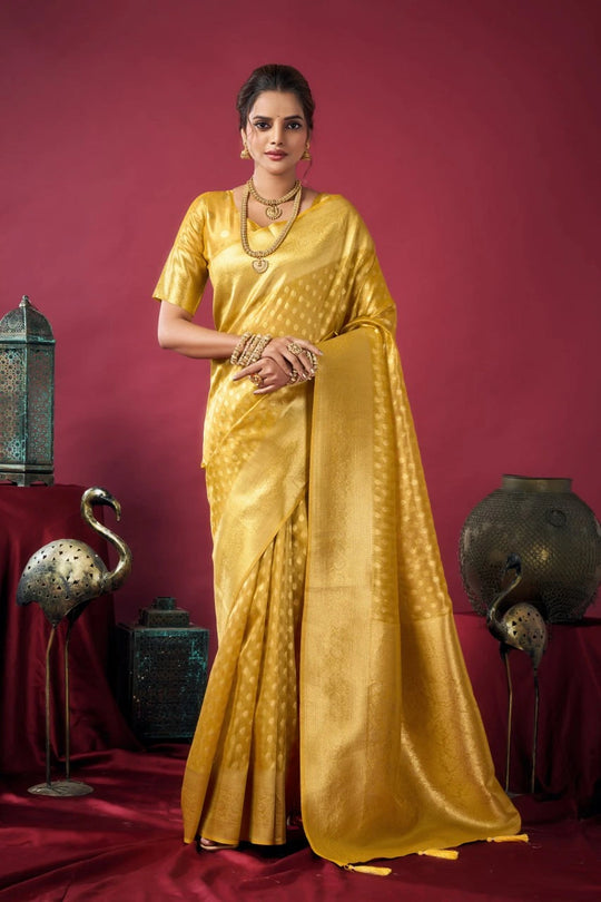 Woman in a yellow saree standing against a red background with decorative elements.