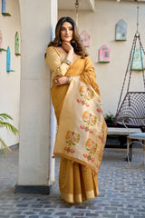 Woman in a yellow saree with floral patterns standing against a wall.