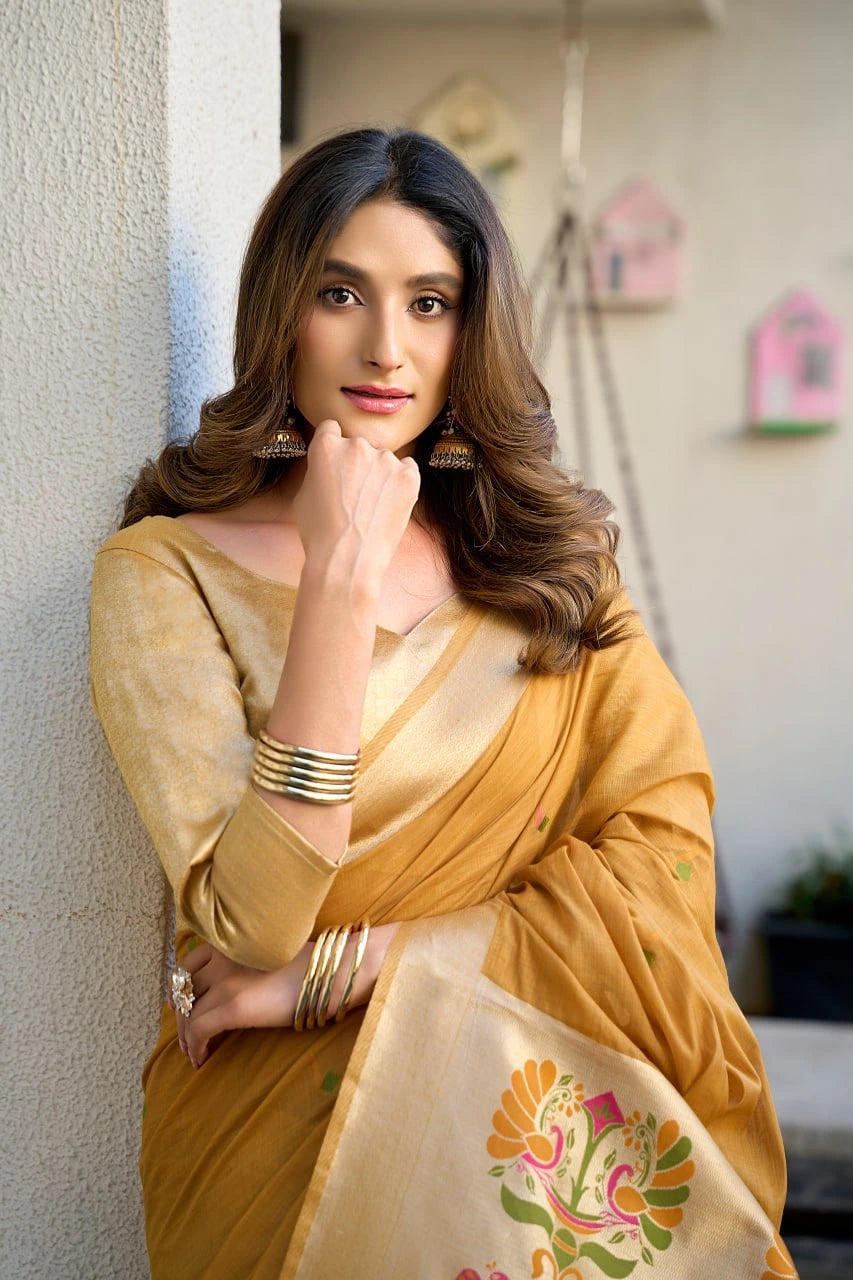 Woman in a yellow saree with floral patterns leaning against a wall.