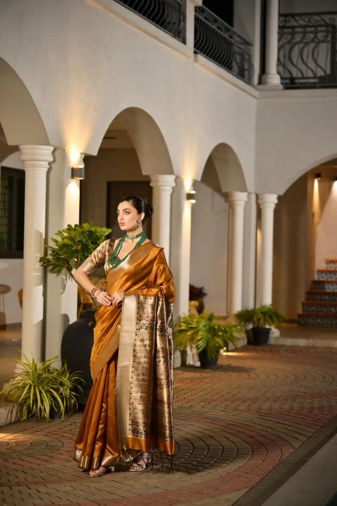 Woman in a traditional saree standing in an elegant indoor setting with arches and plants.