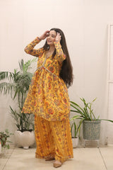 Woman wearing a yellow floral outfit standing indoors with plants in the background