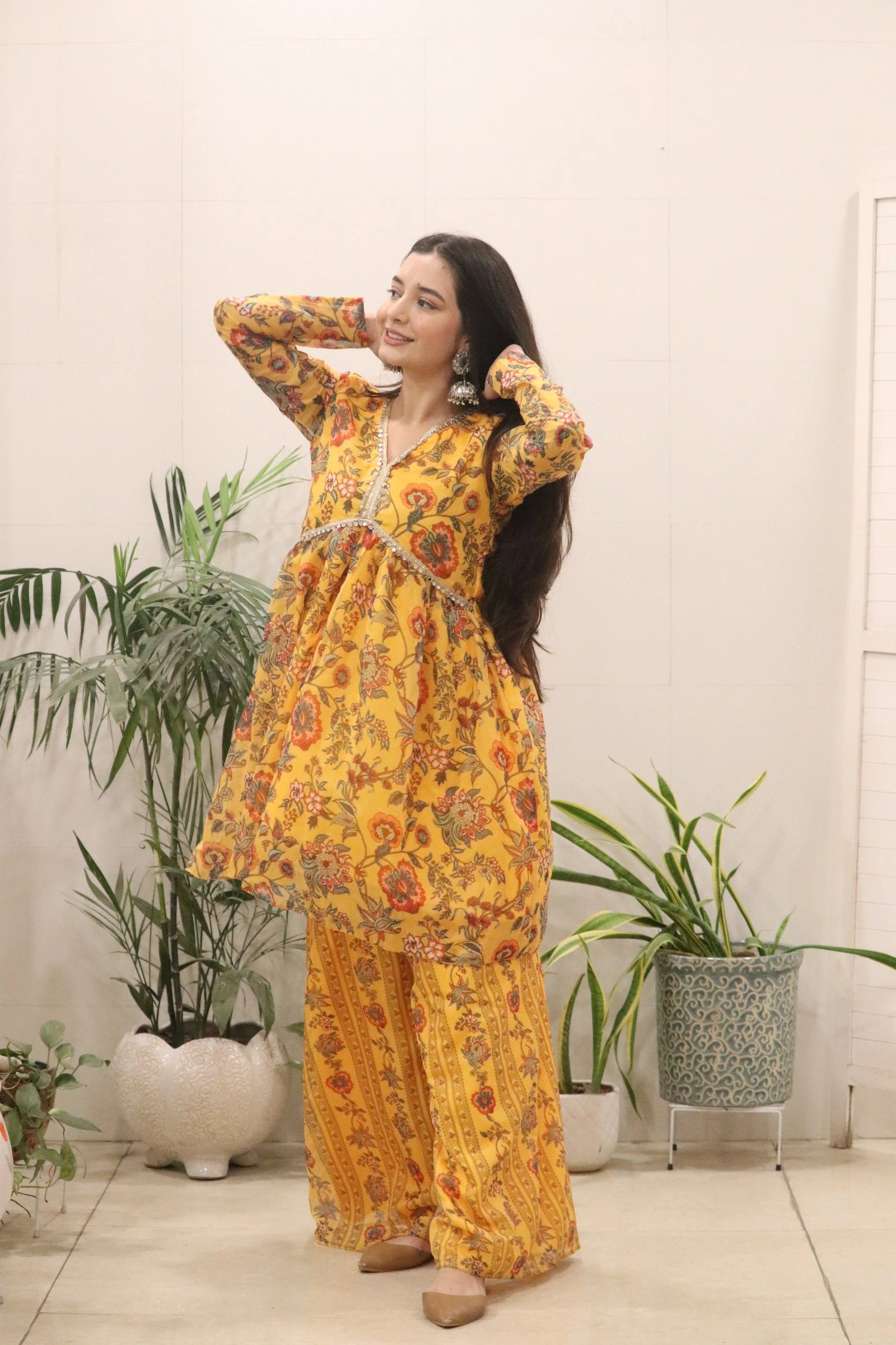 Woman in a yellow floral outfit standing indoors with plants in the background