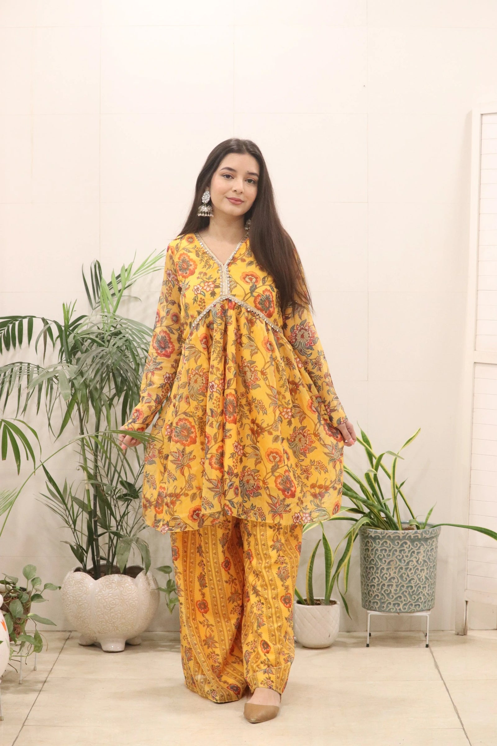 Woman wearing a yellow floral outfit standing in a room with plants.