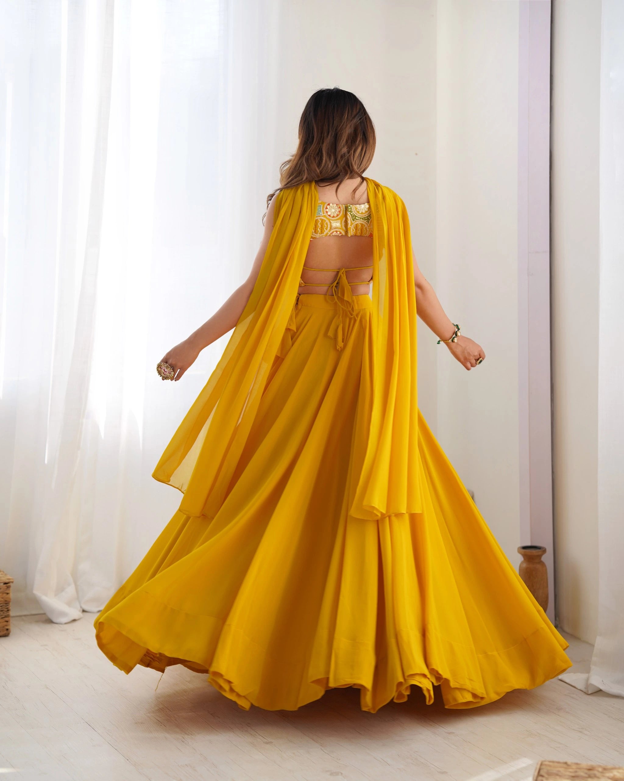 Woman in a yellow saree with a gold blouse against a white curtain background