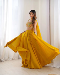 Woman in a yellow traditional outfit with a floral top, standing against white curtains.