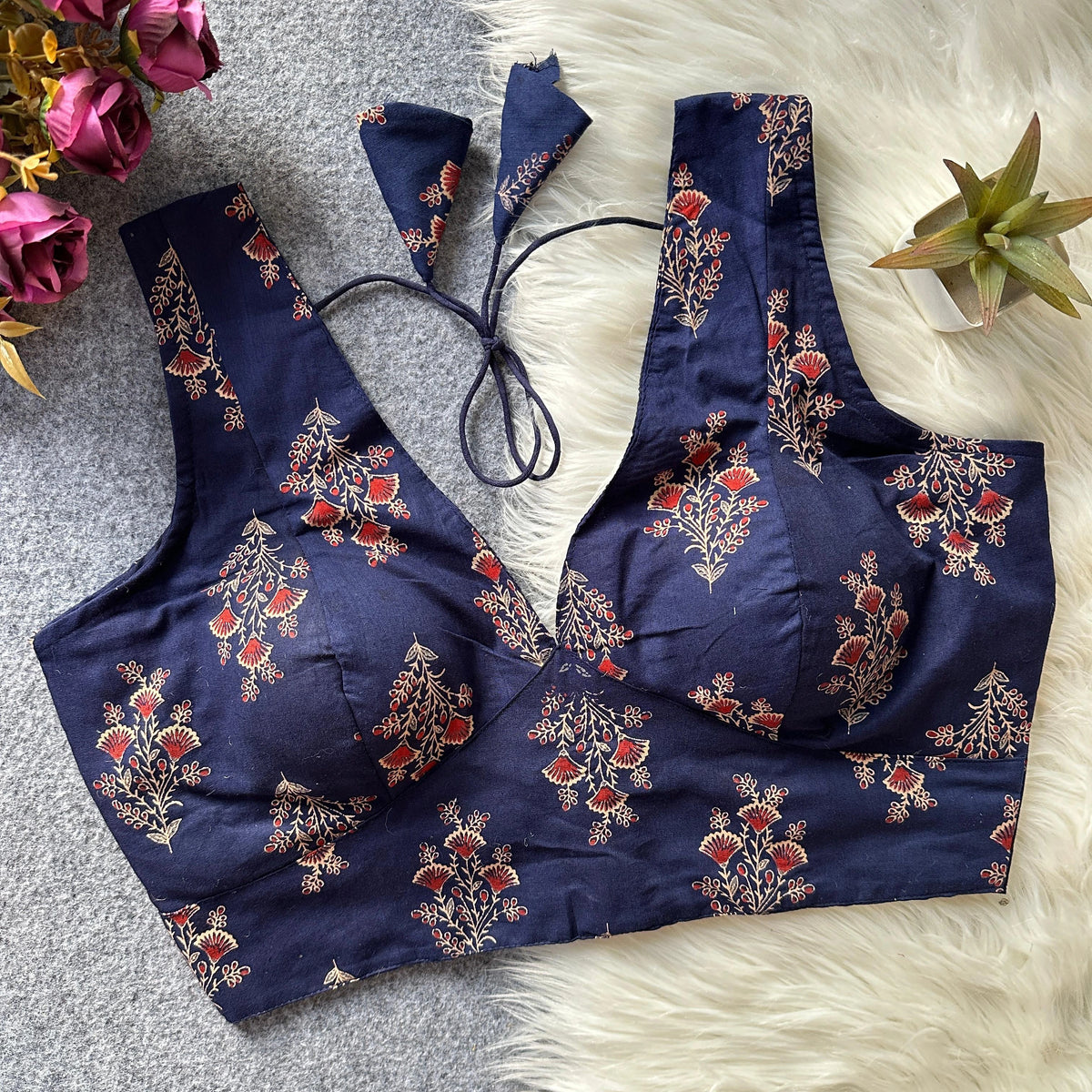 Navy blue embroidered top on a textured surface with flowers and a plant in the background