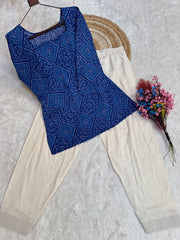 Blue patterned top and beige pants on a textured surface with a hat and flowers.