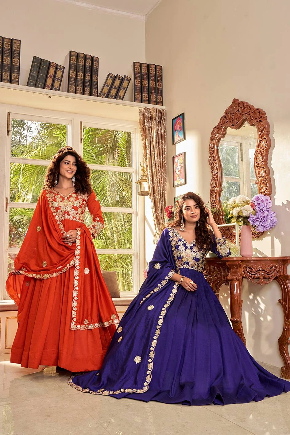 Two women in traditional outfits standing in a room with a mirror and window.