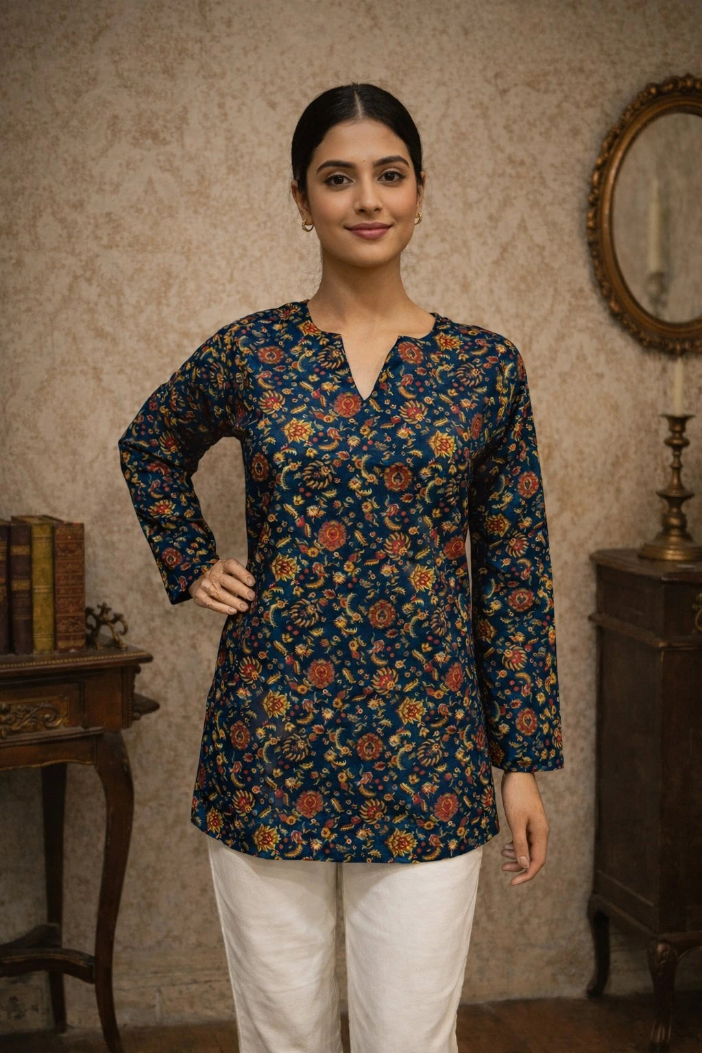 Woman wearing a floral patterned top in a room with a mirror and books.