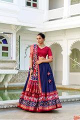 Woman in a traditional red and blue saree standing in an architectural setting.
