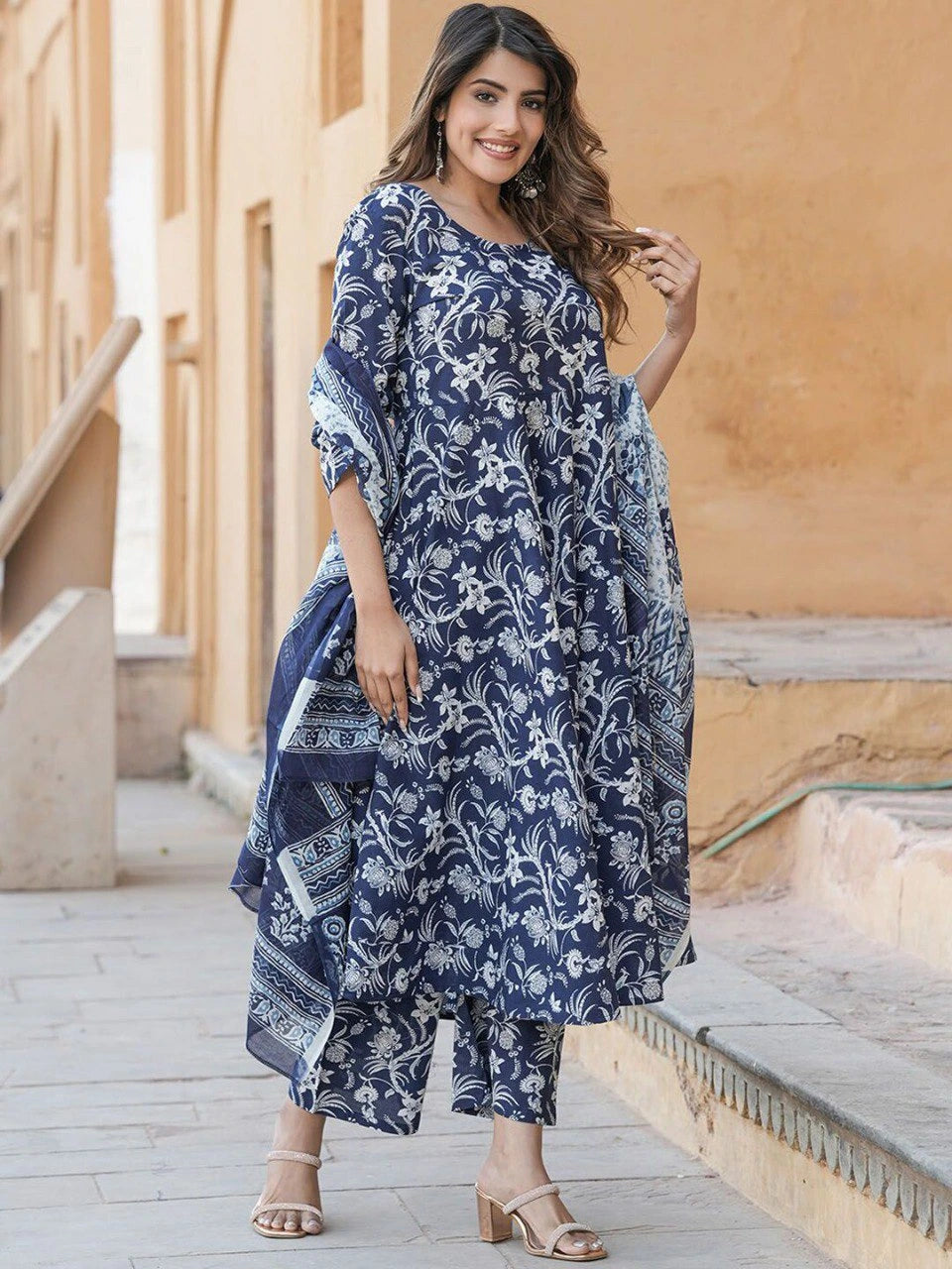 Woman wearing a blue floral dress standing in front of a beige wall.