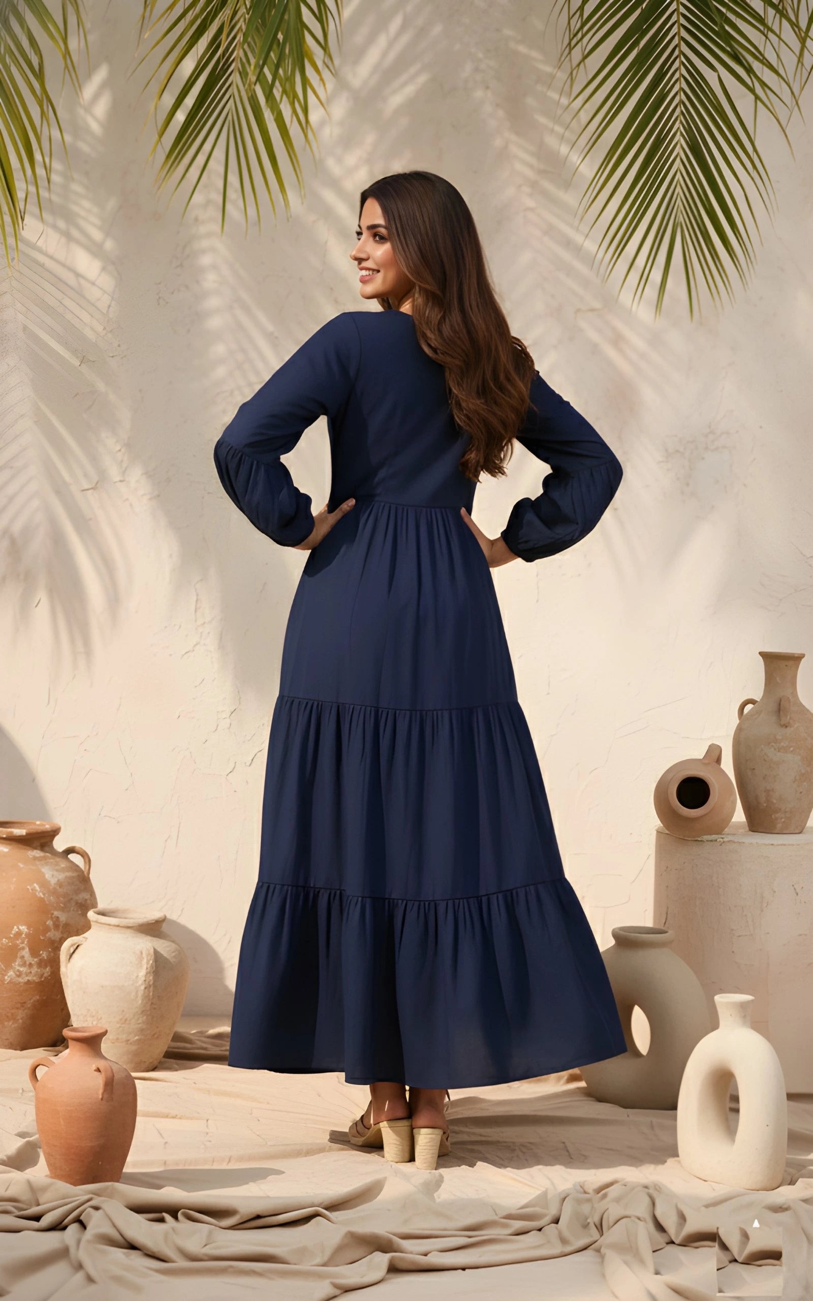 Woman in a navy blue dress standing among decorative vases with palm leaves in the background