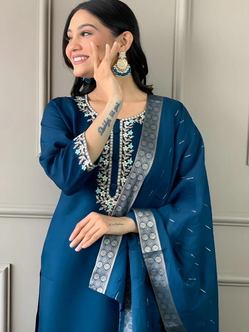 Woman wearing a blue traditional outfit with intricate designs against a neutral background