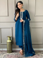 Woman in a blue traditional outfit with a matching dupatta against a neutral wall.