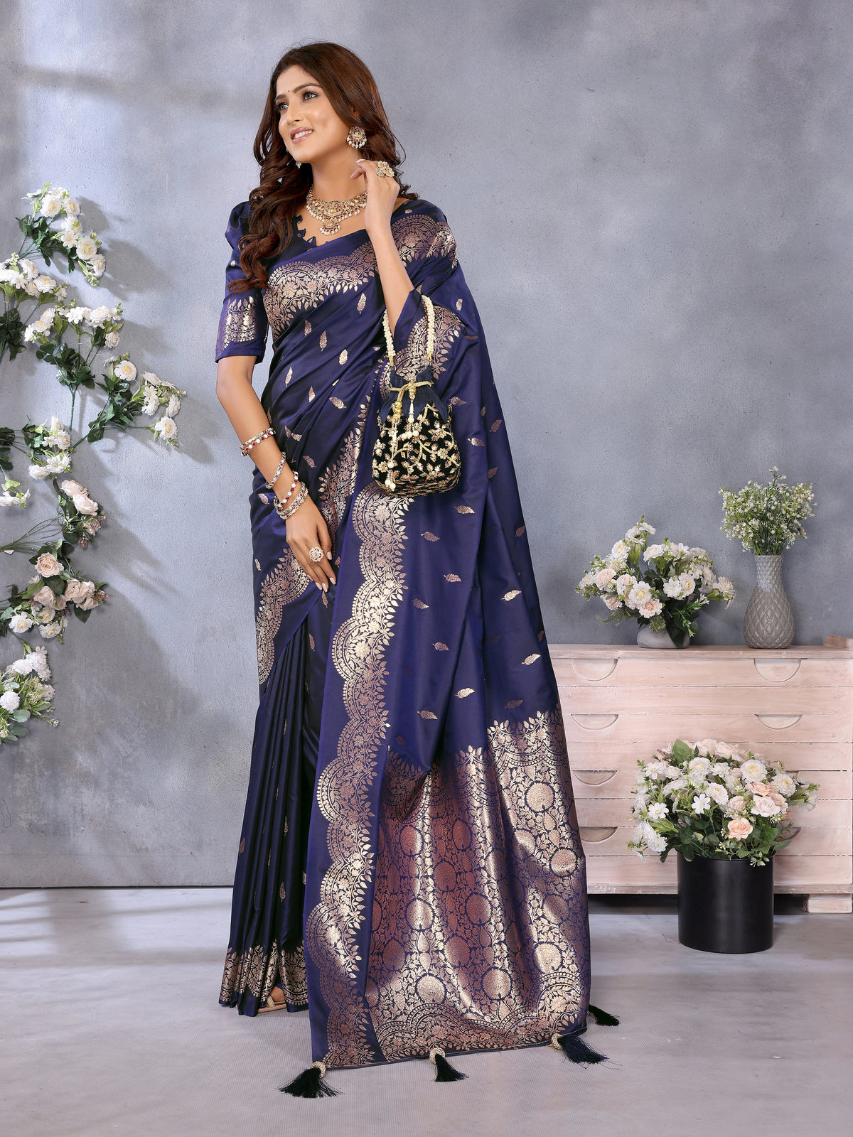 Woman in a blue saree with gold patterns standing in a decorated room.