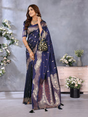 Woman in a blue saree with gold patterns standing in a decorated room.